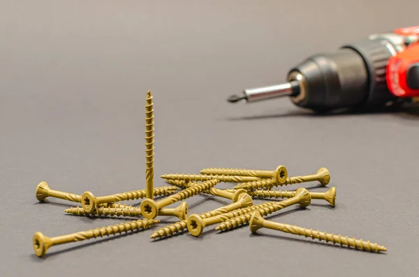 Self-tapping screws on the background of a battery screwdriver, a selection of different self-tapping screws on a black background — Stock Photo, Image