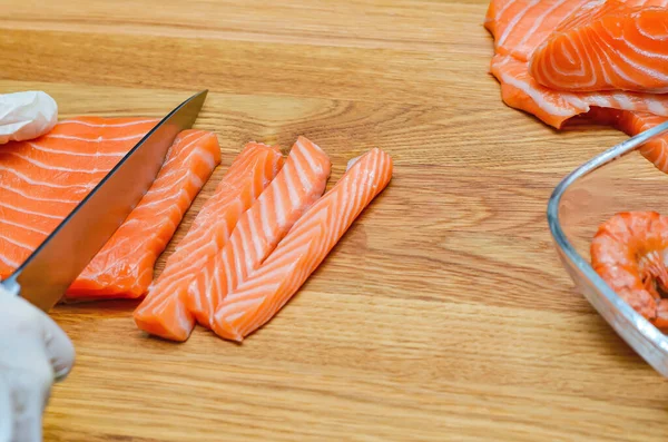 Mâinile bucătarilor sunt aproape. Pe o placă de tăiere din lemn, bucătarul taie un pește roșu cu un cuțit . — Fotografie, imagine de stoc