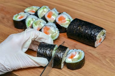 Japon suşisi yapma süreci. Eldeki bıçak ahşap bir tahtaya yakın çekimde bir rulo keser..