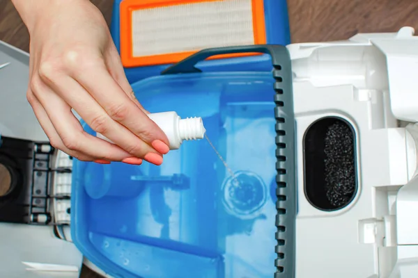 Water foaming agent for vacuum cleaner with water filter. Woman pours liquid from foaming into a container with water of a washing vacuum cleaner