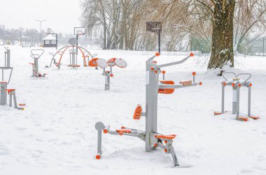 Dayanıklı eğitim ekipmanlarıyla spor sahası. Kışın spor simülatörleri. Parkta kar yağışı.
