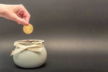 Yatırımlar, kripto para birikimi. Bitcoin elinde, dişi eli altın bir bitcoin parayı bozuk para kavanozuna koyar. dijital para, metin için yer