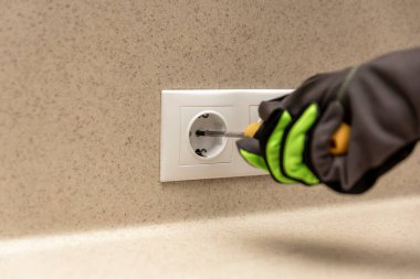 Elektrik prizleri kuruluyor. Elektrikçi elektrik prizlerine dekoratif bir çerçeve takıyor. Tornavida, eldivenli soket takan bir ustanın elinde.