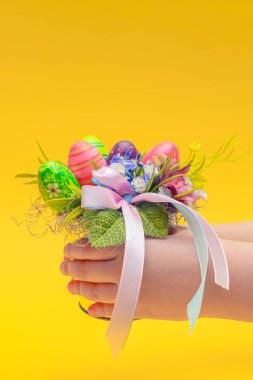 Paskalya kartpostalı. Paskalya için süsleme buketi bir çocuğun elinde. Çocuklar sarı arka planda bir buket tutuyorlar. Mesaj için yer. Dikey fotoğraf