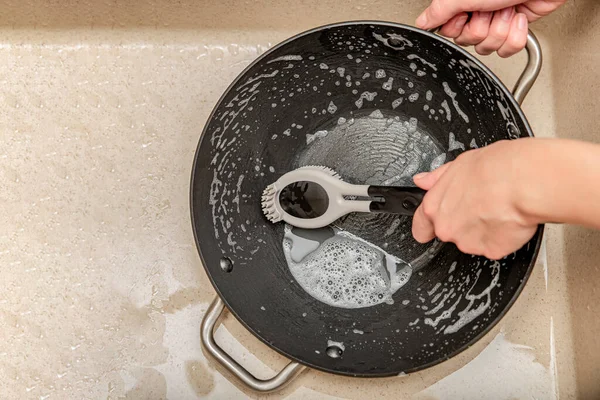 Kobieta myje patelnię, ręka myje patelnię w zlewie kuchennym, silikonowa szczotka do mycia naczyń w kobiecej ręce. Miejsce na tekst — Zdjęcie stockowe