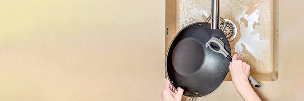 Una mujer lava una sartén, una mano lava una sartén en un fregadero de cocina, un cepillo de silicona para lavar los platos en una mano de mujer. Lugar para el texto — Foto de Stock