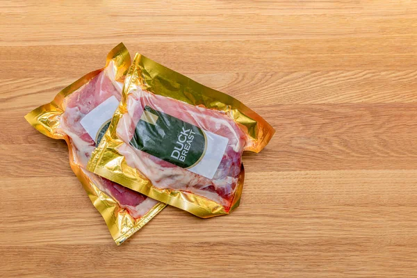 Filetto d'anatra sottovuoto. Carne di anatra sotto vuoto imballaggio di plastica su un tagliere di legno, sfondo per un tema culinario, posto per il testo. — Foto Stock