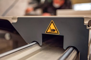 Ahşap işçiliği makinesinde bir uyarı işareti. Marangozluk atölyesinde üretim güvenliği. Sarı üçgende hareket eden parçaların tehlike işareti