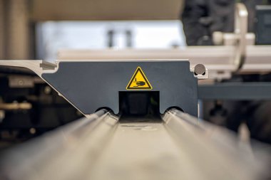 Ahşap işçiliği makinesinde bir uyarı işareti. Marangozluk atölyesinde üretim güvenliği. Sarı üçgende hareket eden parçaların tehlike işareti