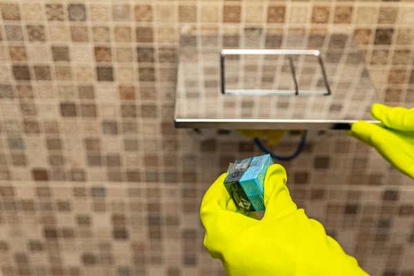 Lavador de cubos de toalete na mão. Uma mão abaixa um cubo desinfetante na água de um vaso sanitário embutido na parede. — Fotografia de Stock