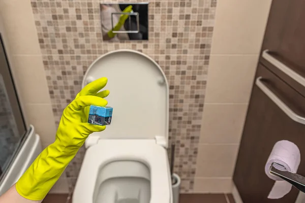 Lavador de cubos de toalete na mão. Uma mão abaixa um cubo desinfetante na água de um vaso sanitário embutido na parede. — Fotografia de Stock