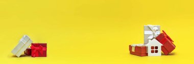 Emlak hediyesi, ev hediyesi. Sarı arka planda hediye kutusundaki beyaz oyuncak evi. Yazdırma için kartpostal, metin için pankart