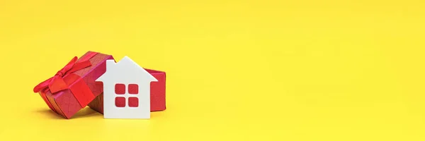 Real estate gift banner. Gift box with house. Real estate concept. White toy house in a gift box on a yellow background. Postcard for printing, banner with place for text. Panoramic photo