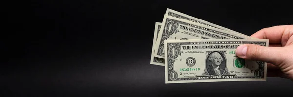 Dinero en mano, billete en mano. Mano sosteniendo un billete de un dólar aislado sobre fondo negro. Banner con un fondo negro sobre temas financieros, lugar para texto. — Foto de Stock