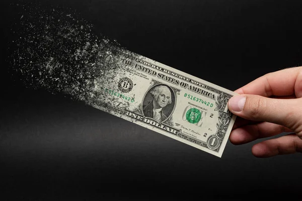 Enflasyon, dolar hiperenflasyonu ve siyah arka plan. Bir dolarlık banknot siyah arka plandaki bir adamın eline sıkılır. Satın alma gücü ve enflasyon kavramı.