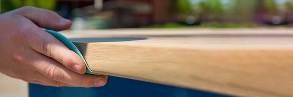 Un menuisier broie une planche de bois avec du papier de verre. Le processus de fabrication de meubles en bois. Mains du maître gros plan. — Photo