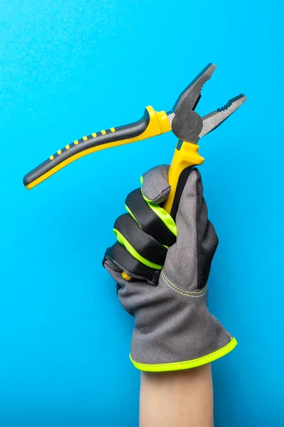 Zangen. Gelbe und schwarze Zangen in der Hand eines Elektrikers auf blauem monochromen Hintergrund. Reparatur und Installation Werkzeug. Banner für die Gestaltung und den Druck von Bauthemen. — Stockfoto