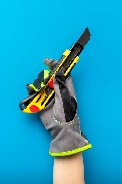 Baumesser vorhanden. Schreibwarenmesser in der Hand mit einem Handschuh auf blauem Hintergrund. Bau- und Renovierungsthema. Platz für Text oder Design — Stockfoto