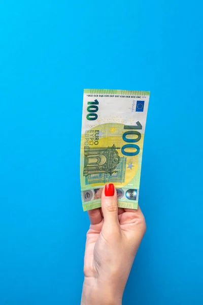 Money in hand, poster with banknote in hand. Hand holding 100 euro banknote isolated on blue background. Banner with blue background on financial themes