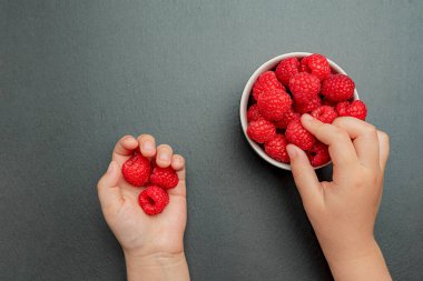 Çocuk bir ahududu aldı ve onu eline koydu. Plakadaki siyah arkaplanda böğürtlenler, metin, tarif veya tasarım eklenecek yer