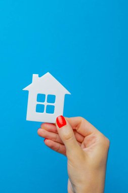 Ev bir hediye. Elinde hediye yayı olan oyuncak evi. Mavi arka planda gayrimenkul hediye konsepti. Yazdırma için kartpostal, metin için pankart.