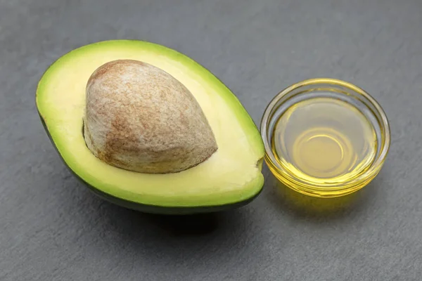 Avocado-olie. Een avocado met een bot ligt op een stenen dienblad. Avocodo-olie wordt in een plaat gegoten. Banner voor bedrukking, etiketontwerp, gezonde voeding. — Stockfoto