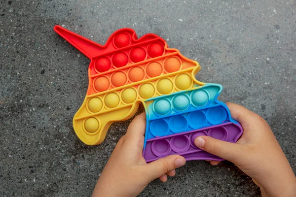 Pop-lo brinquedo, cores do arco-íris, na forma de um unicórnio. Colorido, multi-colorido, sensorial anti-stress brinquedo fidget pop-lo em mãos das crianças — Fotografia de Stock