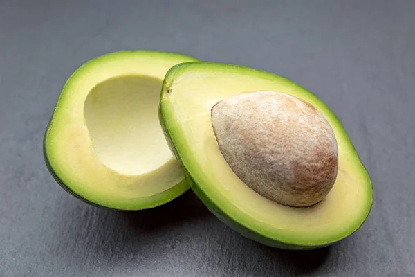 Taze avokado ikiye bölünmüş. Kemikli bir avokado siyah bir taş tepside yatıyor. Sağlıklı gıda konsepti. — Stok fotoğraf