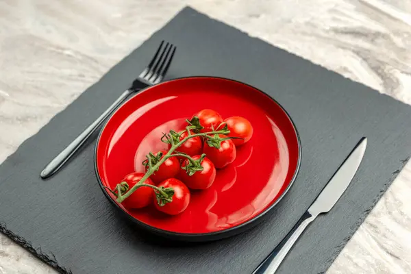 Tomaten auf dem Teller als Diät oder gesundes Ernährungskonzept. Kirschtomaten auf einem roten Teller mit Gabel und Messer auf schwarzem Steingrund. Platz für Text oder Design — Stockfoto