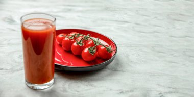 Bir bardak domates suyu ve bir dal küçük domates pankartı. Kırmızı tabakta mermer kaplama domatesler. Metin ya da tasarım eklenecek yer