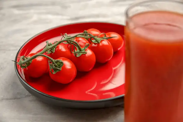 Ein Glas Tomatensaft und ein Zweig kleiner Tomaten. Kirschtomaten in einem roten Teller auf einem Marmorgrund. Platz zum Einfügen von Text oder Design — Stockfoto