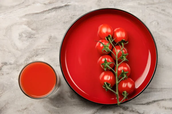 Un vaso de jugo de tomate y una rama de pancarta de tomates pequeños. Tomates cherry en un plato rojo sobre un fondo de mármol. Lugar para insertar texto o diseño —  Fotos de Stock