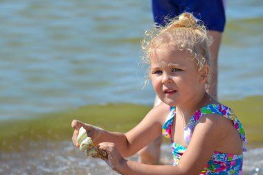 Deniz kenarında dinlen. Küçük kız kumsalda kumla oynuyor. Kız deniz kenarında oyuncaklarla oynuyor