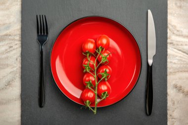 Domates diyeti. Kırmızı tabakta, siyah zemin üzerinde olgun kırmızı domatesler. Diyet konsepti ve az miktarda yiyecek..