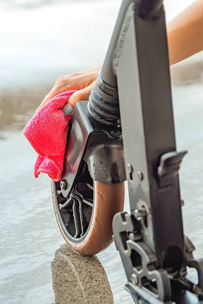 Limpeza ou lavagem da scooter. Cuidado scooter elétrico. Uma mulher limpa uma scooter com um pano depois de lavar com água. Lugar para texto — Fotografia de Stock