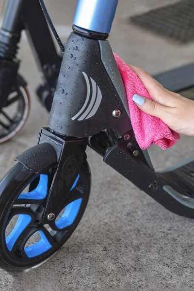 Limpieza o lavado del scooter. Cuidado de scooter eléctrico. Una mujer limpia un scooter con un trapo después de lavarlo con agua. Lugar para el texto —  Fotos de Stock