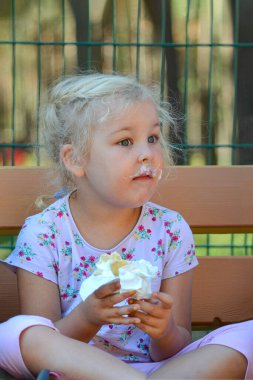 Girl 5 years old eats ice cream in a summer park on a bench. The girl smeared her face with ice cream.