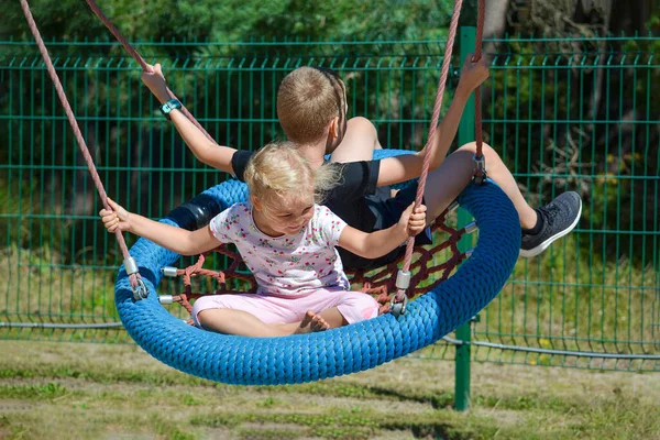 Gyerekek hintáznak. Fiú és lány hintáznak a parkban egy nyári napon. Hintázz a vidámparkban. banner szöveggel — Stock Fotó