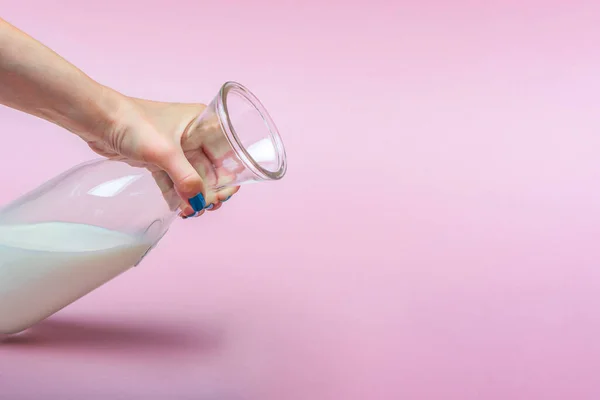 Una brocca di latte su uno sfondo rosa in una mano di donne. Latte in bottiglia di vetro. Spazio per testo, grande banner. — Foto Stock