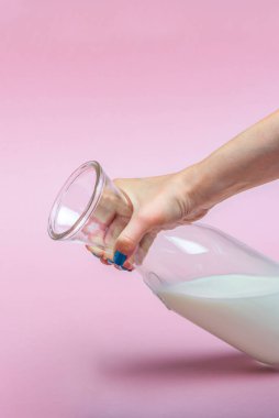 Bir sürahi süt pembe arka planda bir kadının elinde. Cam şişedeki süt. Metin için boşluk, büyük pankart.