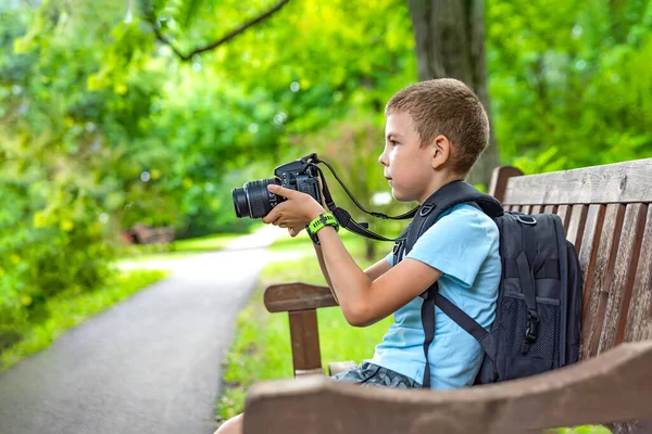 Tourist mit Kamera. Ein Junge mit einer Kamera fotografiert die Natur im Park. Ein junger Fotograf sitzt auf einer Parkbank und fotografiert die Natur. Unterwegs mit der Kamera — Stockfoto