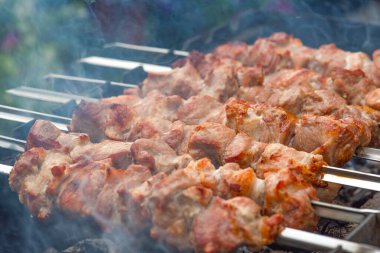 Mangal yapmak, ızgara et barbeküsü. Metal şişler üzerinde domuz şiş pişirmek. Tabağın üzerinde közden çıkan duman birikiyor. Fotokopi alanı olan reklam panosu