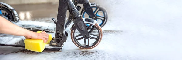 Rengör skotern. Elektrisk skotervård. En kvinnlig hand tvättar en skoter med en svamp med skum i en biltvätt.. — Stockfoto