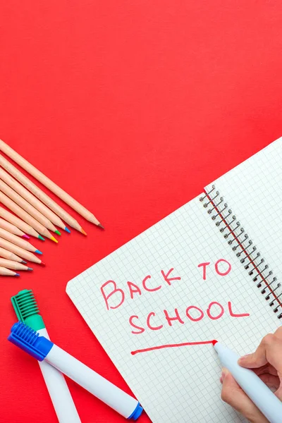 Je retourne à l'école. L'enfant écrit Retour à l'école dans un cahier en marqueur rouge. Le concept du début de l'année scolaire. bannière pour le site sur un fond rouge. — Photo