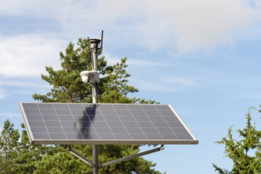 Solar powered surveillance camera. Solar panels powering a surveillance camera in a city park against a background of blue sky. Safety and clean energy concept clipart