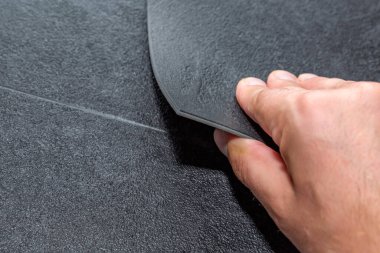 Döşeme seçimi. Tadilat ya da inşaat konsepti. Dokulu vinil döşemeli fayans tutan bir erkeğin yakın çekimi. Plastik ve vinil döşeme örnekleri.