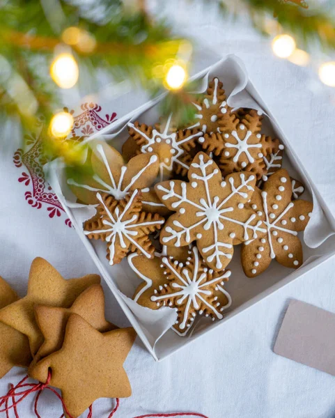 Yıldızlar şeklinde zencefilli kurabiye ve kremayla süslenmiş kar taneleri beyaz bir kutuda yatıyor. Noel hediyesi olarak beyaz bir arkaplanda zencefilli kurabiye. Odakta olmayan bir Noel ağacı.