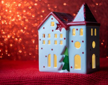 Parlak pencereli küçük bir evin şenlikli bir figürü. Noel süsleri. Yeni yıl. Mutlu Noeller ve yeni yıl, tebrik kartı. Kırmızı arka planda dekoratif bir ev ve altın bir bokeh. Boşluğu kopyala.