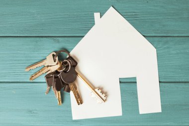 Eski turkuaz ahşap arka planda gümüş anahtarlarla kesilmiş ev sembolü kağıt. Yeni ev konsepti. Yeni bir daire alıyorum. Kira ve kira