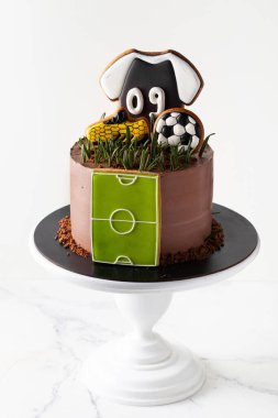 Beyaz arka planda futbol temalı doğum günü pastası. Futbol topu, bot ve tişört şeklinde zencefilli kurabiye..